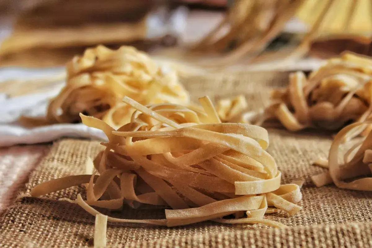 Nidi di tagliatelle fatte in casa, pronte per essere cucinate. La pasta fresca, con la sua texture rustica, è disposta su una tela grezza, invitando a un pasto autentico.