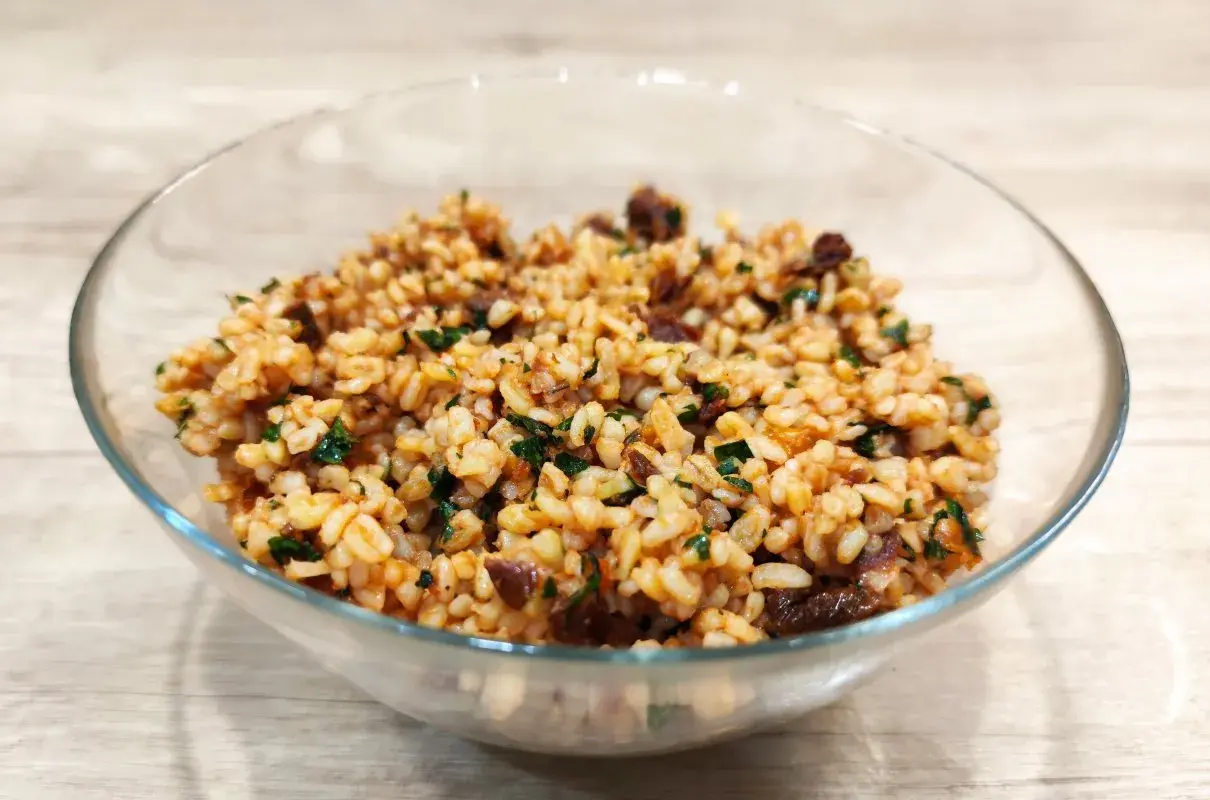 Sałatka z kaszą bulgur i suszonymi pomidorami, pełna smaku i ziół, w szklanej misce.