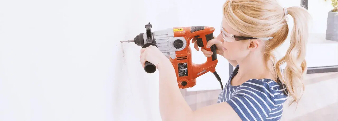 Femme avec lunettes de protection utilisant un marteau-perforateur pour percer du béton.