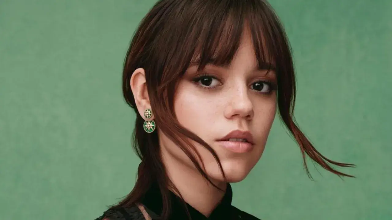 Jenna Ortega z kolczykami w kształcie gwiazdek. Jej włosy są ciemnobrązowe, a tło zielone.