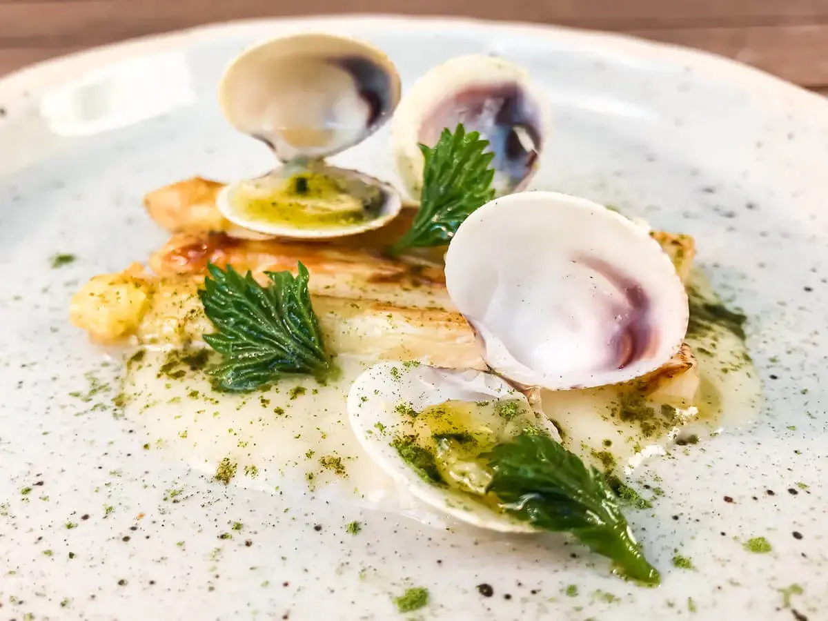 Delizioso piatto con pesce bianco, gamberi e **lupini di mare** in una salsa cremosa, guarnito con erbe fresche.