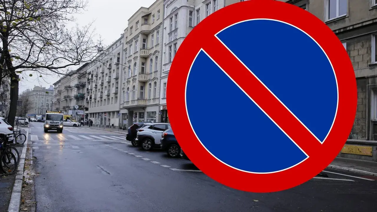Znak B35 zakazu zatrzymywania się na mokrej ulicy z samochodami i kamienicami w tle.