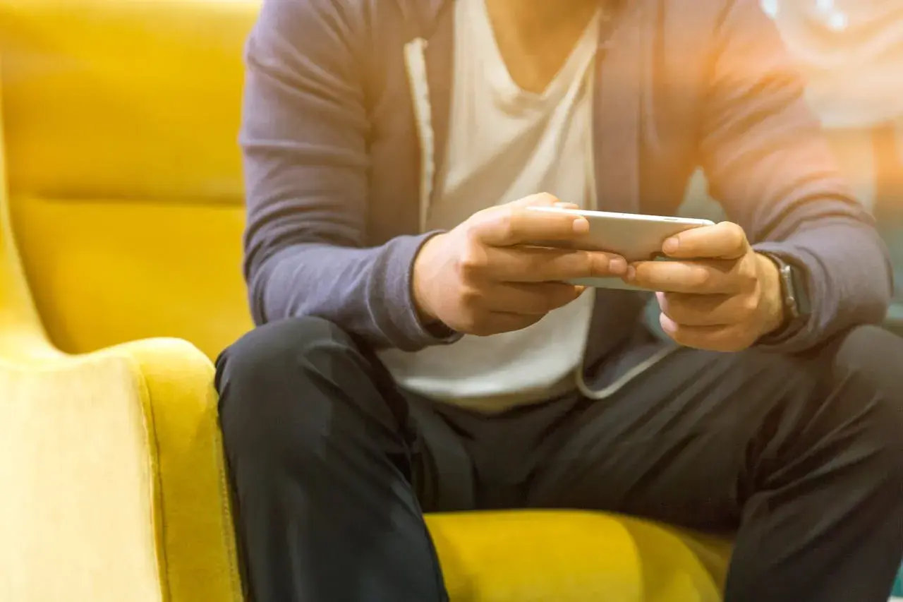 Mężczyzna siedzi na żółtym fotelu, grając na telefonie. Nawet poza siecią, jego **tuya smart** urządzenia działają bez zarzutu.