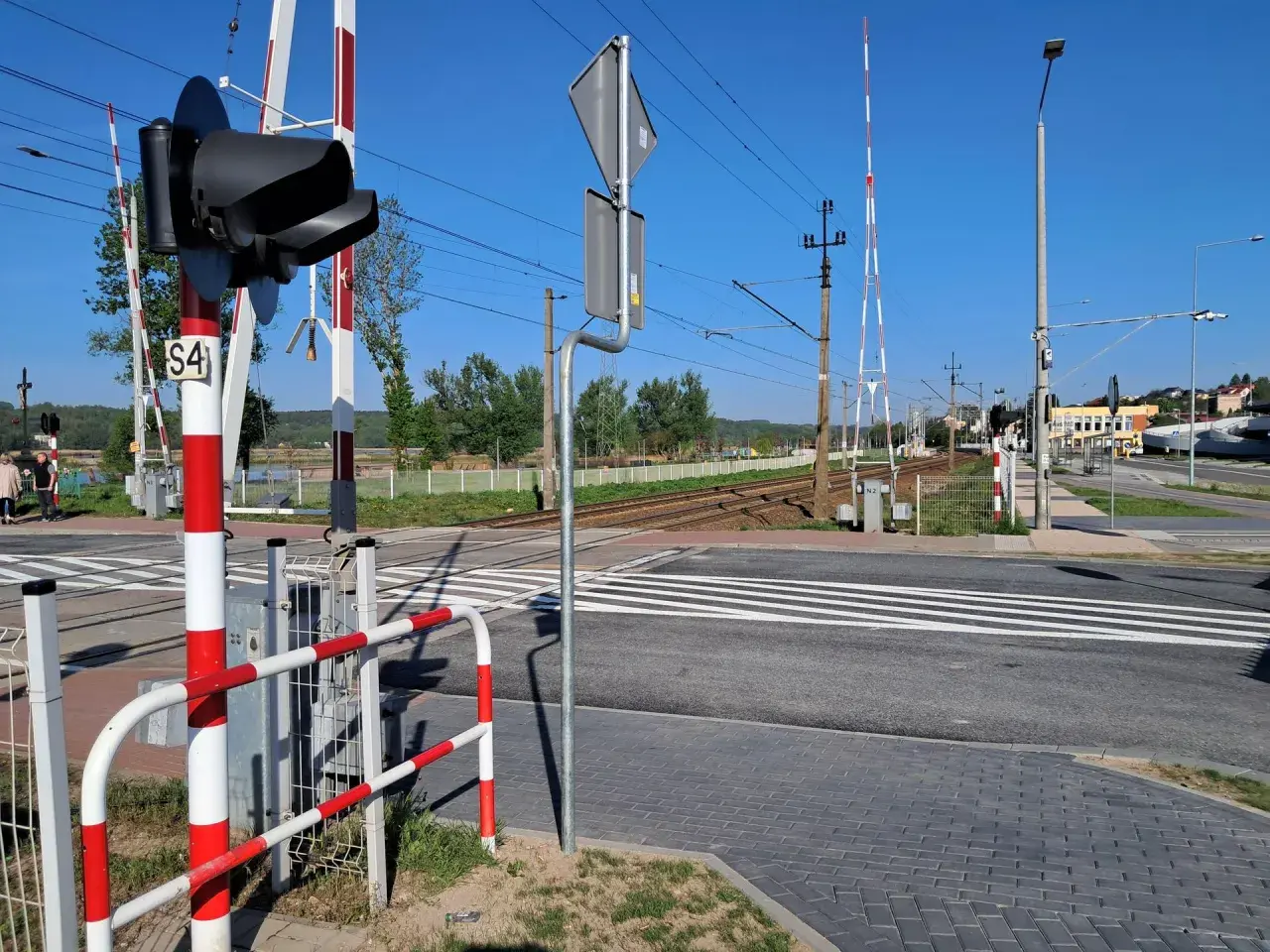 Sygnalizacja świetlna i rogatki na przejeździe kolejowym. Czekam na pociąg, by móc bezpiecznie przejechać.