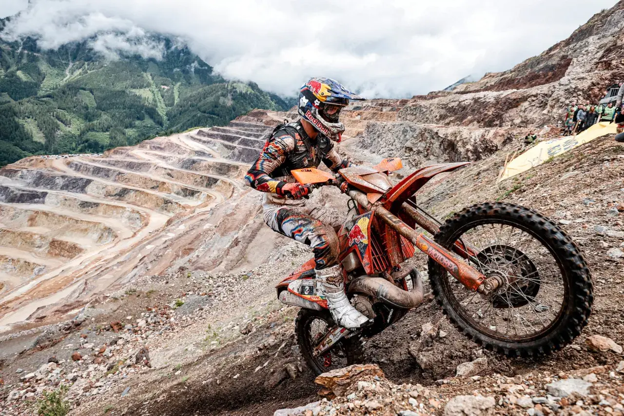 Motocyklista hard enduro na pomarańczowym motocyklu w kopalni odkrywkowej.