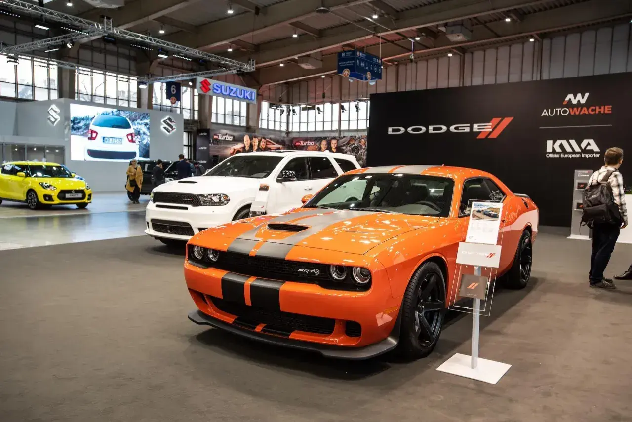 Pomarańczowy Dodge Challenger SRT na wystawie, obok białego Durango. Sprawdź dodge challenger cena i dostępne modele.