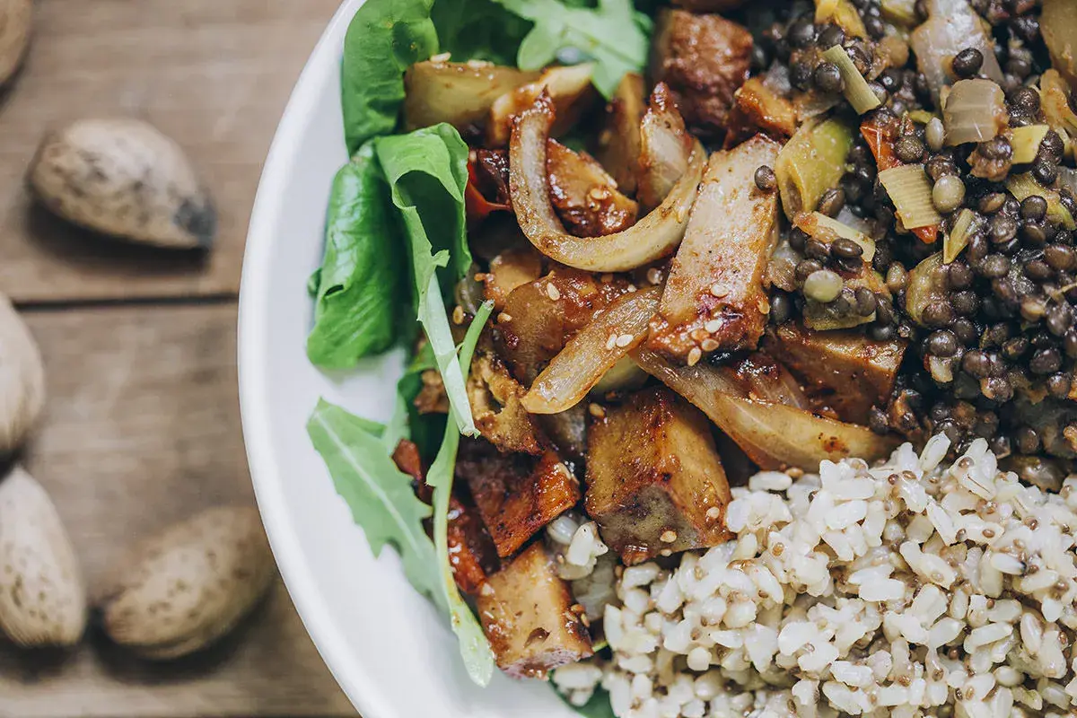 Plato con seitan salteado, lentejas, arroz integral y hojas verdes. Una deliciosa opción para tus recetas de seitan.