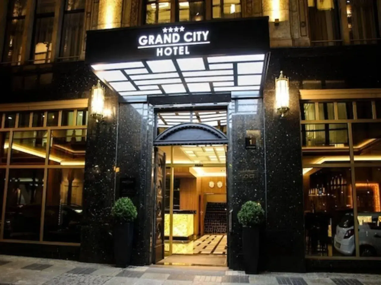 Elegancki **grand city hotel** nocą, z podświetlanym neonem i lśniącym wejściem.