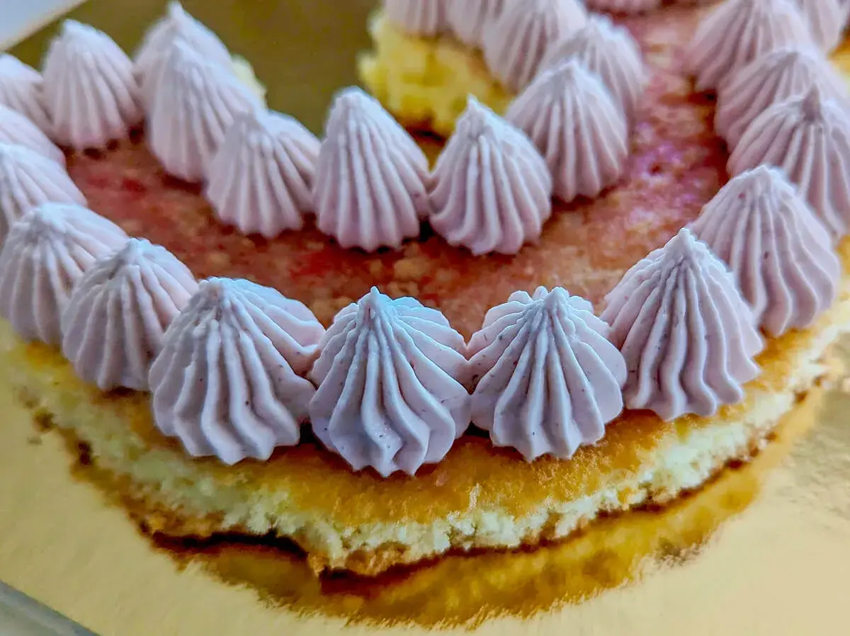 Gâteau rond décoré de rosaces de ganache framboise sur un lit de fruits rouges.