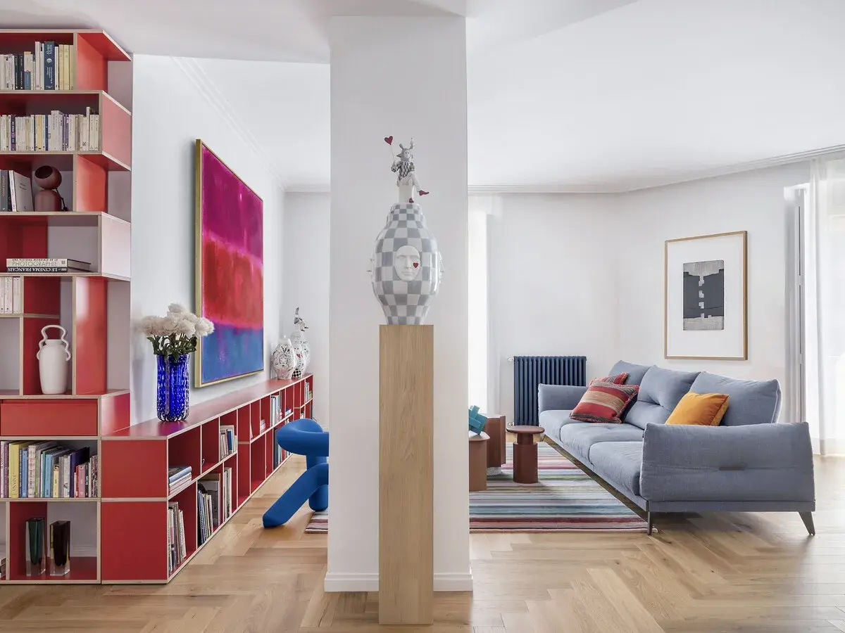 Estudios de arquitectura: sala de estar moderna con sofá azul, alfombra de rayas, estanterías rojas y arte abstracto.