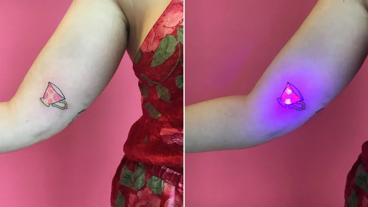 Uroczy tatuaż filiżanki z kwiatami, który pod wpływem światła UV staje się magicznym, fluorescencyjnym dziełem sztuki.