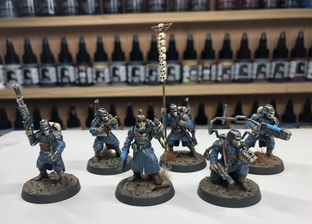 Krieg command squad w niebieskich mundurach, z karabinami i sztandar z czaszkami, gotowi do walki.