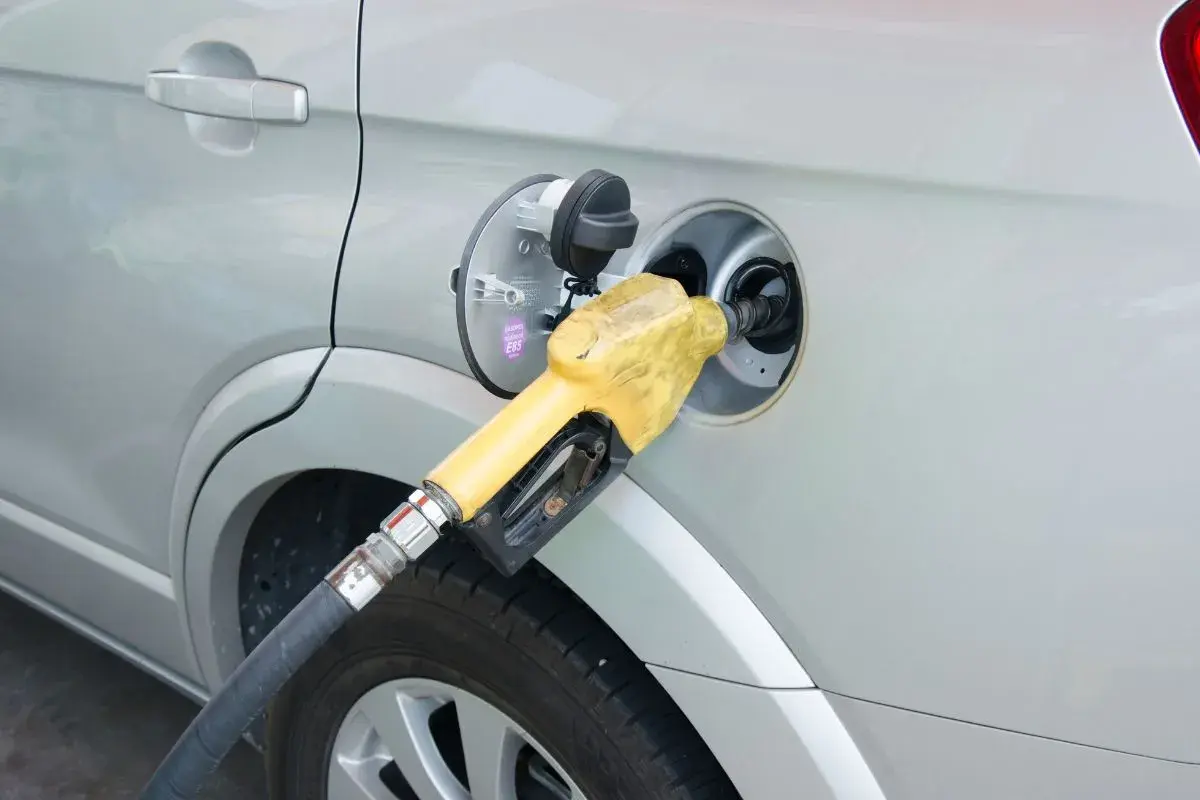 Żółta dysza dystrybutora paliwa wlewana jest do baku srebrnego samochodu. Prosty sposób, jak zatankować auto.