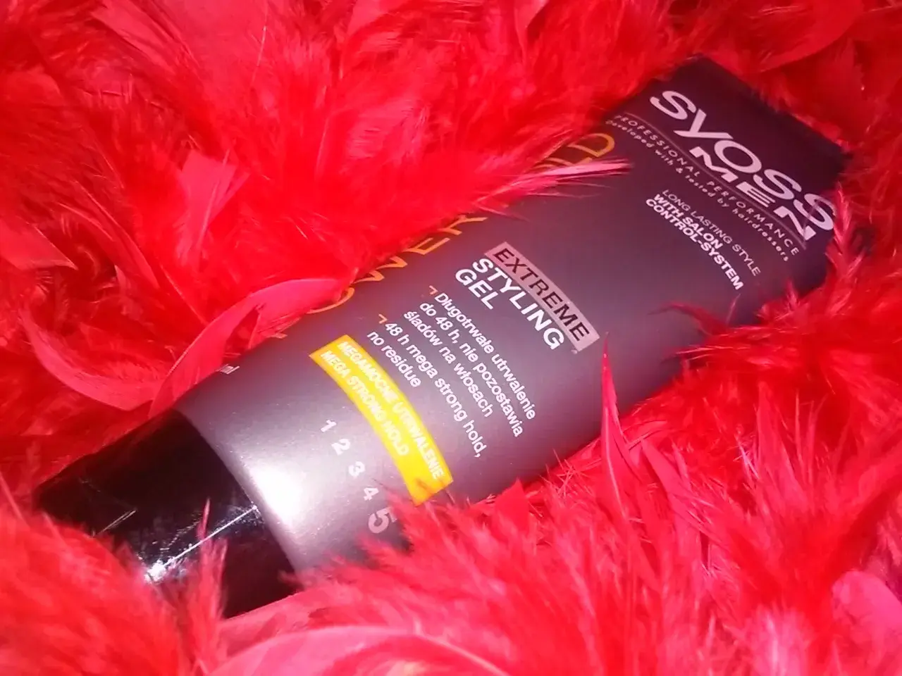 Syoss Men Extreme Styling Gel, dla mega mocnego utrwalenia włosów na żel, otoczony czerwonymi piórami.