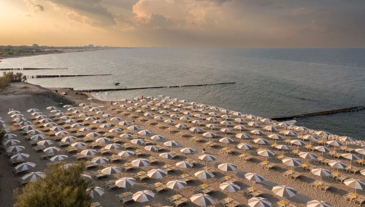 Filetto di ombrelloni e lettini sulla sabbia dorata, con il mare calmo e il cielo crepuscolare a fare da sfondo. Un'immagine che evoca la tranquillità dei **Marche mare**.