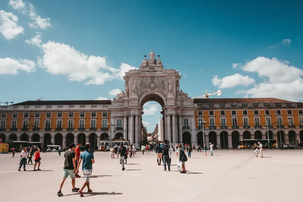 En solig dag på ett stort torg i Lissabon, Portugal. Människor promenerar under en imponerande triumfbåge. Ett perfekt restips för Portugal.