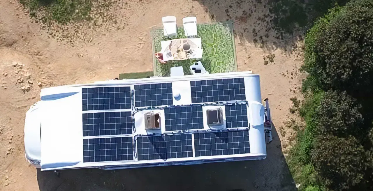 Kamper z panelami słonecznymi na dachu, idealny do życia w stylu instalacja off grid. Na zewnątrz stolik z kawą i krzesła.