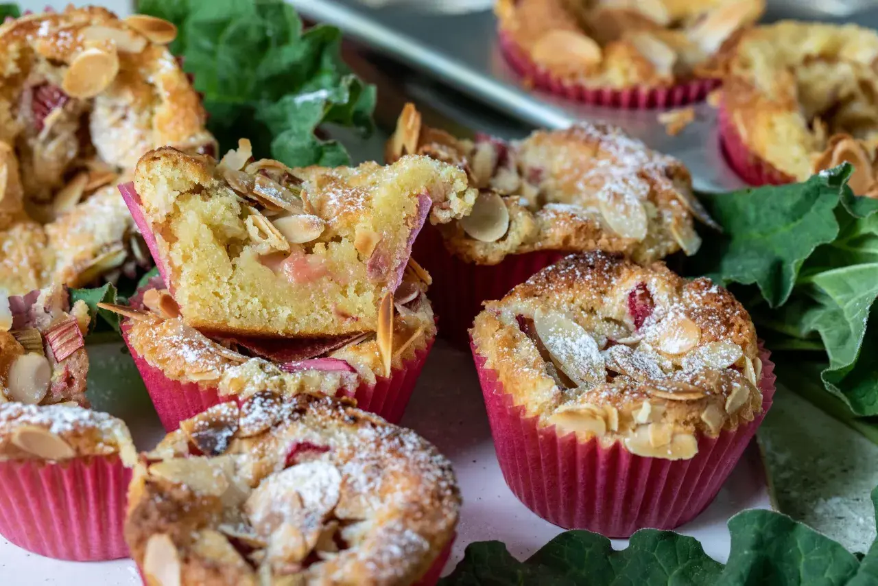 Fluffiga rabarber muffins med mandelflagor och pudersocker, bakade i rosa muffinsformar.