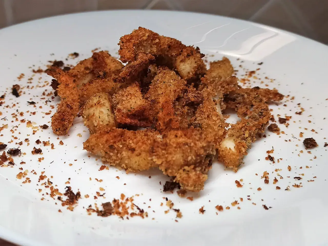 Un mucchietto di seppie gratinate al forno, dorate e croccanti, su un piatto bianco.