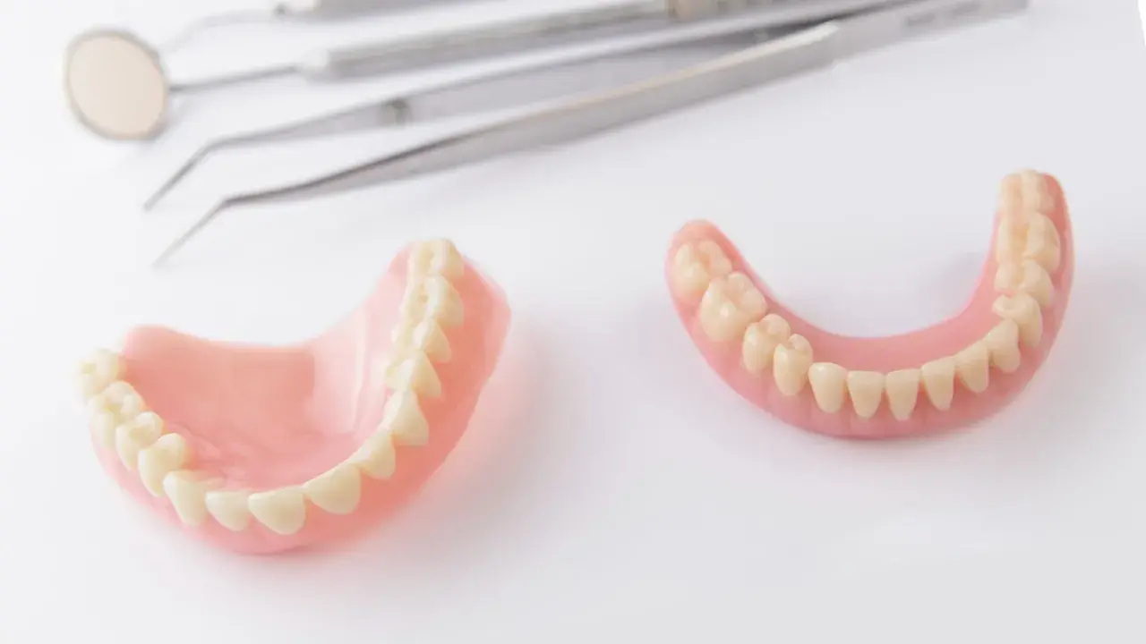Protesi dentarie, superiori e inferiori, su sfondo bianco, con strumenti dentistici sfocati sullo sfondo. Soluzione per denti mobili.