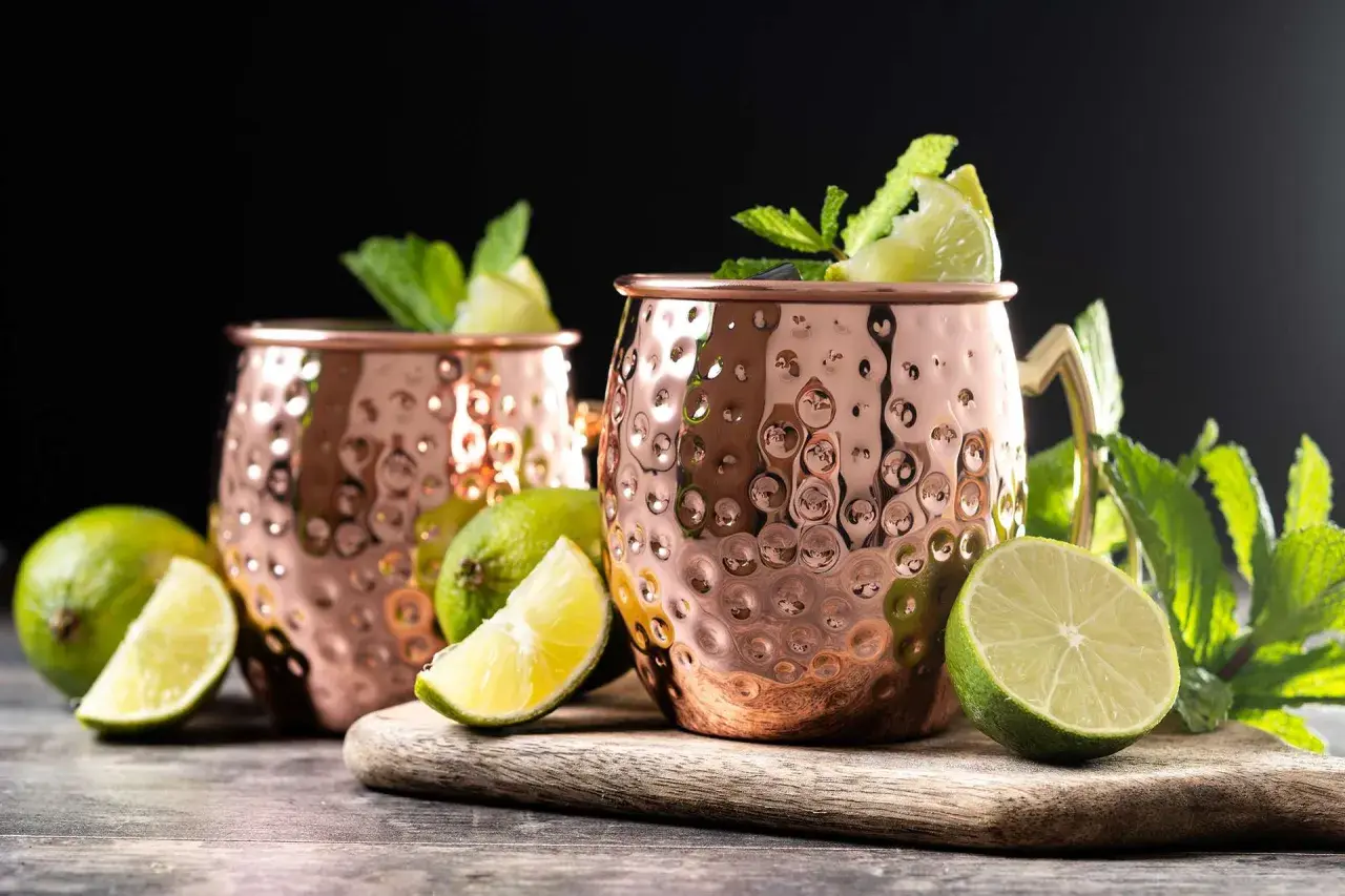 Due tazze di rame martellato per un Moscow Mule, guarnite con menta fresca e spicchi di lime.