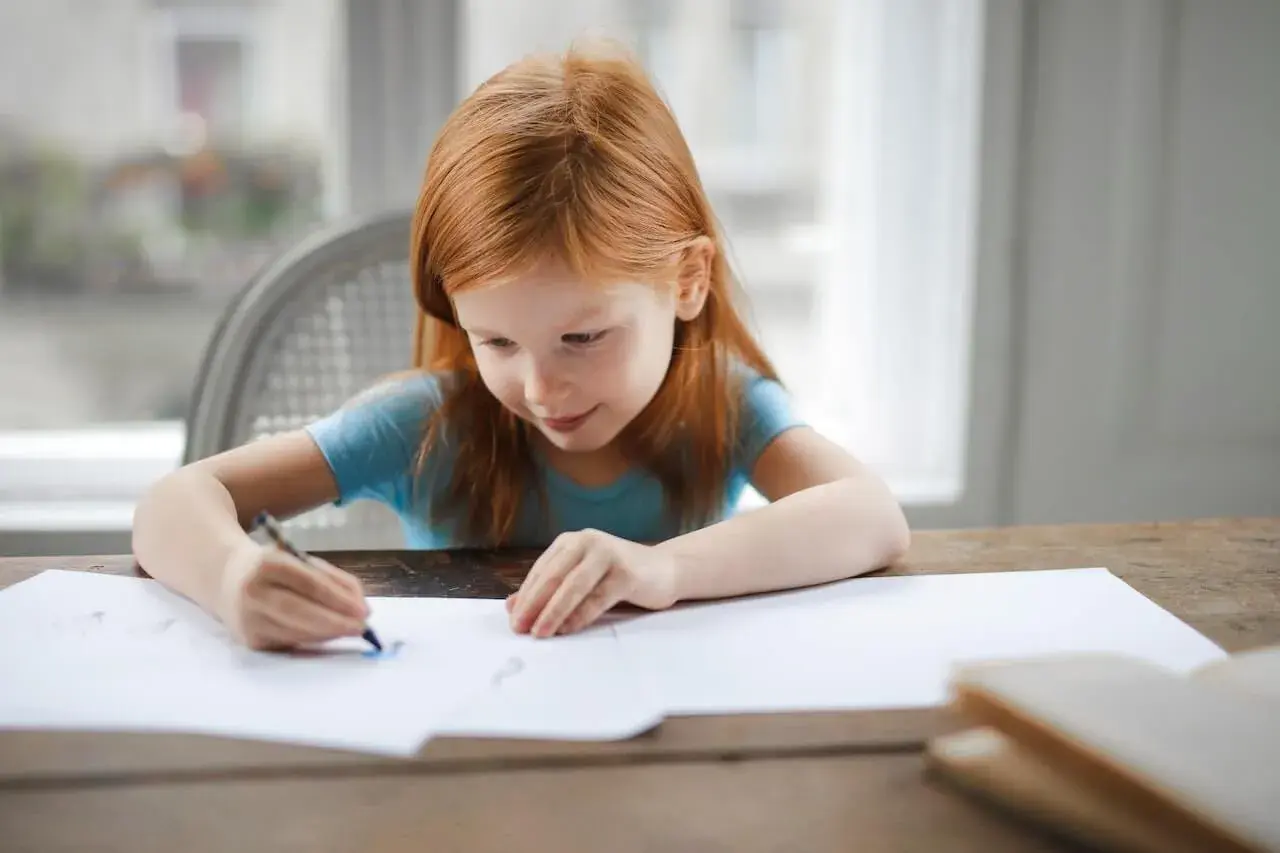 Ruda dziewczynka rysuje. Jej skupienie i zaangażowanie to cechy, które doceni każdy pedagog specjalny, posiadający odpowiednie kwalifikacje.