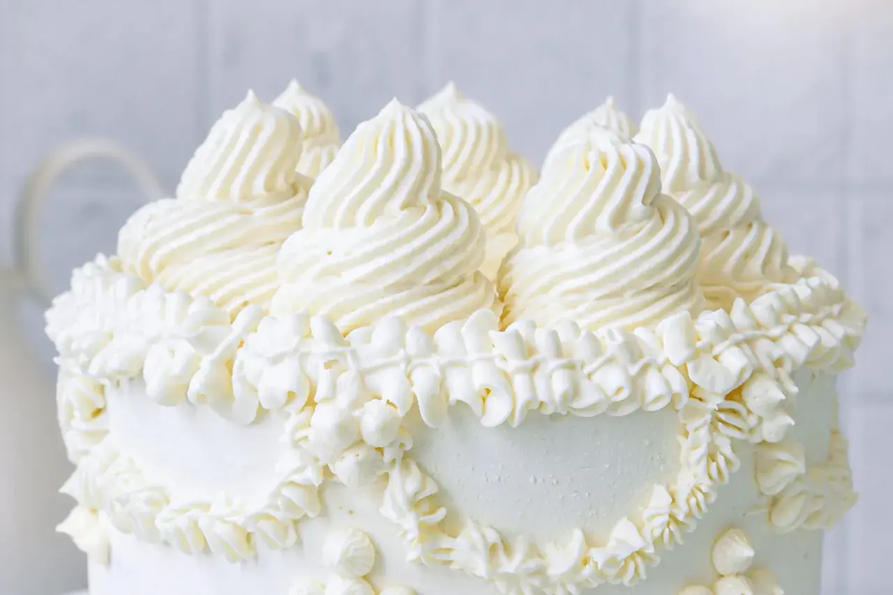 Ein weißer Kuchen, üppig dekoriert mit amerikanischer Buttercreme in kunstvollen Tupfen und Rüschen.