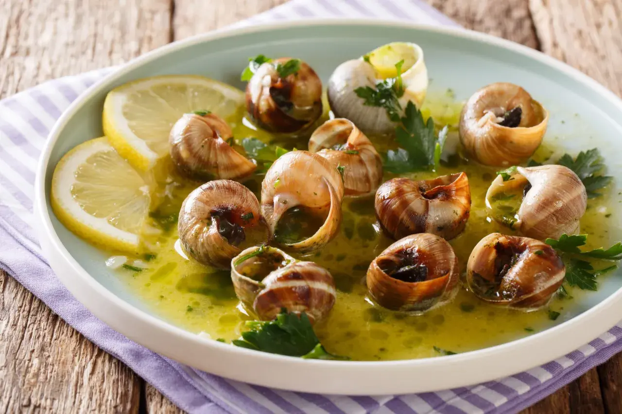 Escargot to danie z gotowanych ślimaków w sosie czosnkowo-ziołowym, podane z plasterkami cytryny.