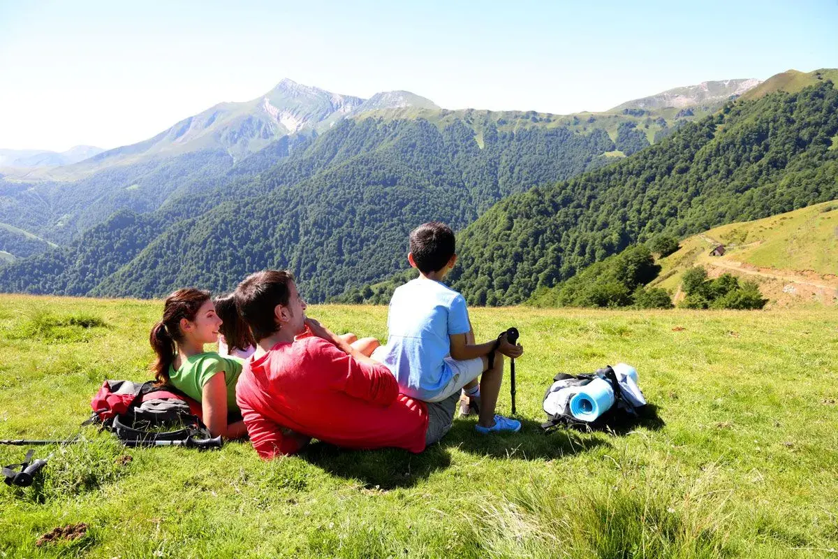 Rodzina odpoczywa na zielonej łące, podziwiając majowe Tatry. W tle gęsty las i skaliste szczyty.