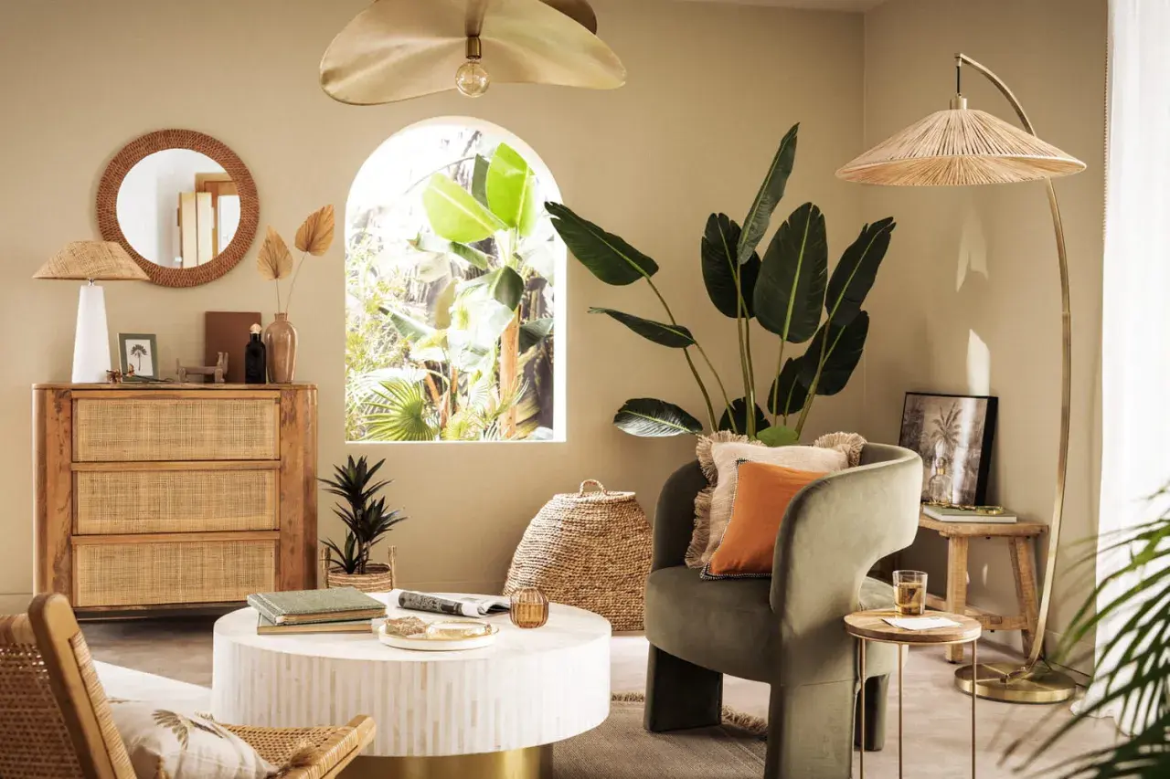 Salon bohème avec meubles en rotin et touches dorées. Le vert du fauteuil et l'orange du coussin s'accordent bien avec le doré.