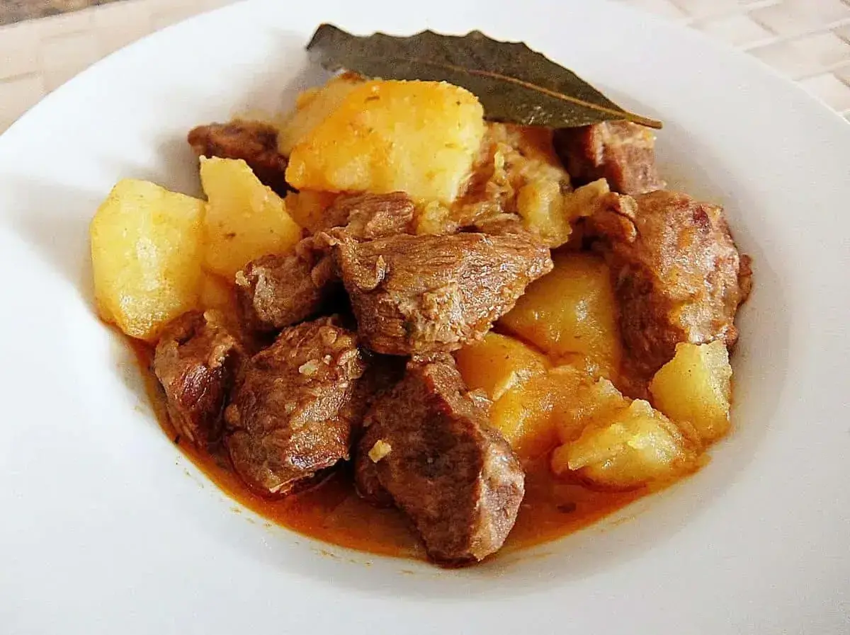 Sabroso morcillo de ternera guisado con patatas y una hoja de laurel, servido en un plato blanco.