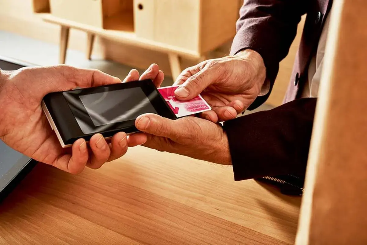Dwie dłonie zbliżają kartę do terminala płatniczego. To prosty sposób, jak doładować telefon na kartę.