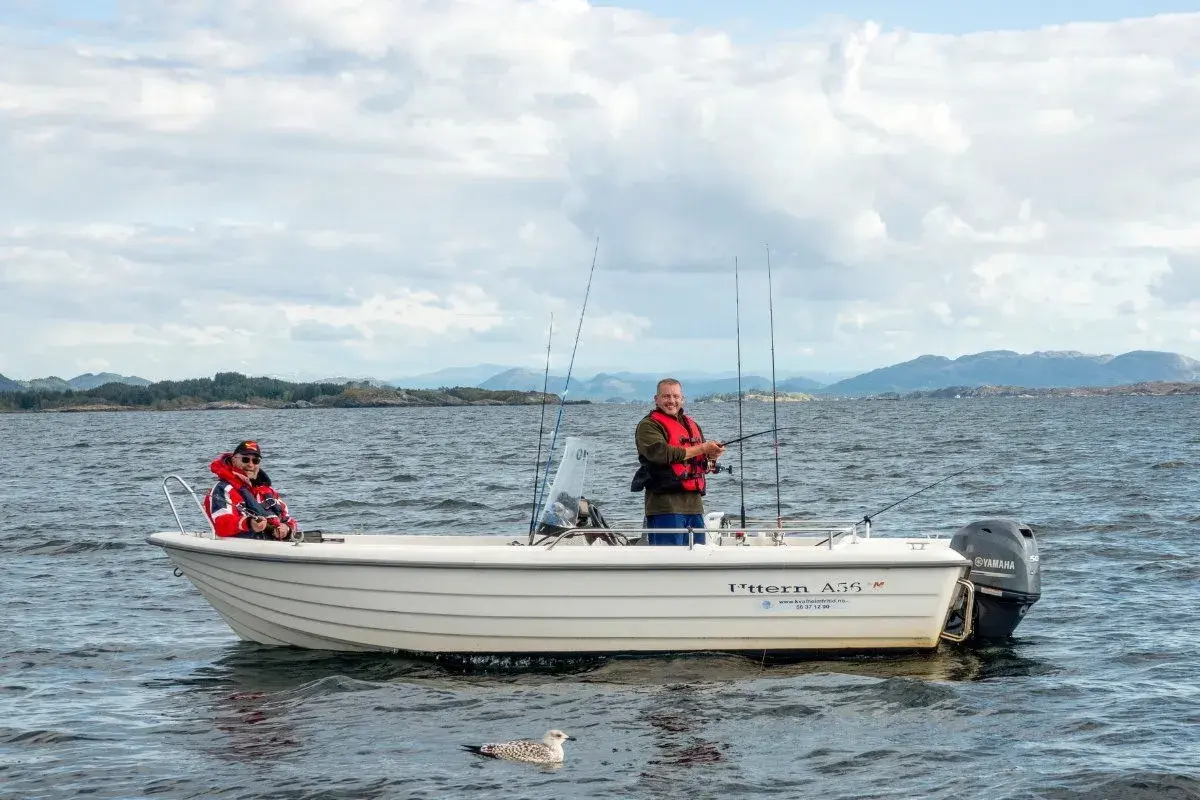 Zwei Männer genießen das Angeln in Norwegen auf einem Boot. Eine Möwe schwimmt im Wasser.