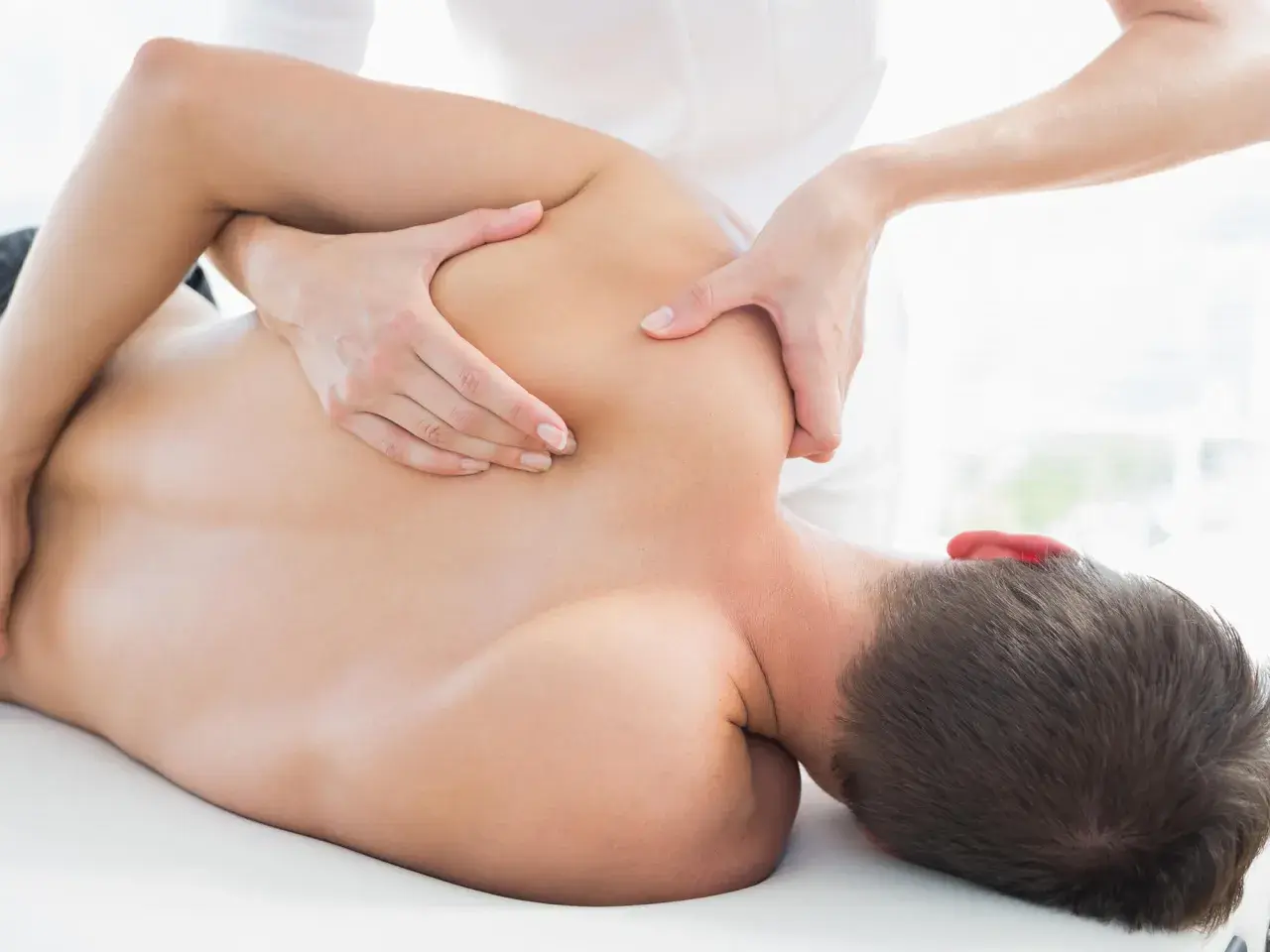 Physiotherapeut behandelt Schulterschmerzen am AC Gelenk eines Mannes mit manueller Therapie.