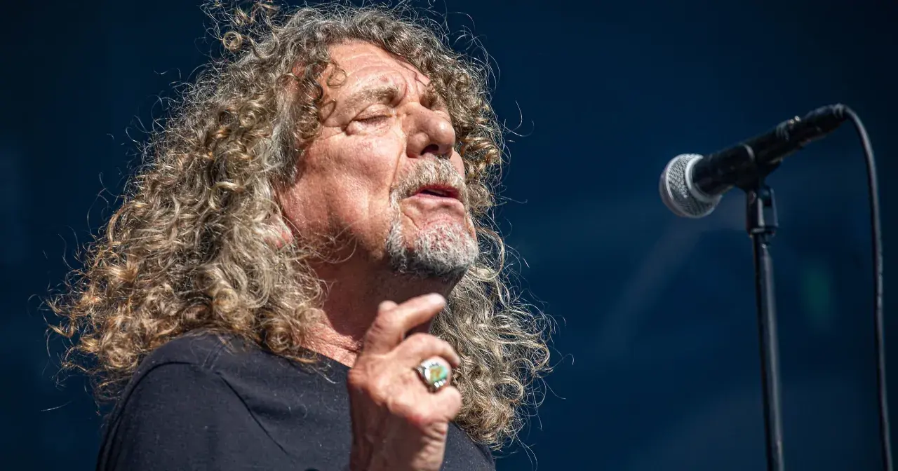 Wokalista Led Zeppelin, Robert Plant, śpiewa do mikrofonu, z charakterystyczną burzą kręconych włosów.