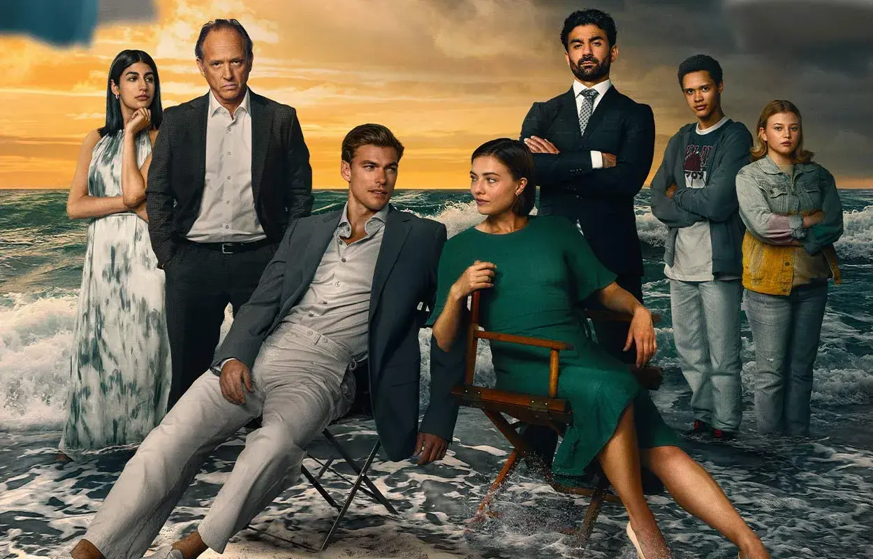 Rollistan i strandhotellet: en familj samlad vid havet, med dramatiska moln och vågor som bakgrund.
