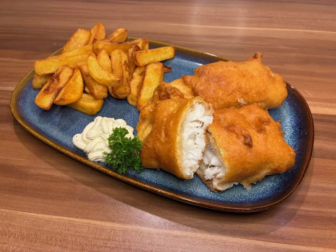 Knuspriges Fish and Chips Rezept: goldbraun frittierter Fisch mit Pommes, dazu Remoulade und Petersilie.