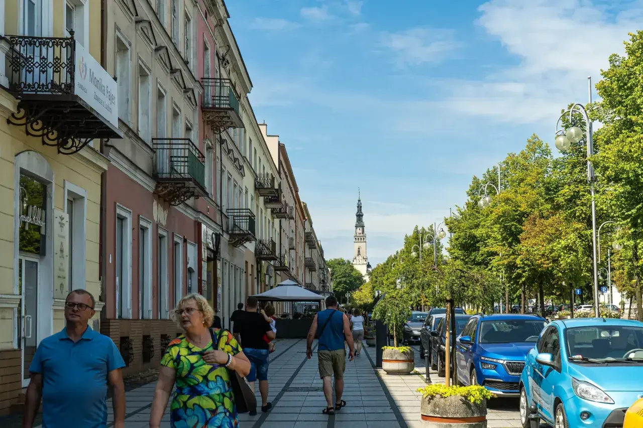 Spacerem ulicą w Częstochowie, w oddali widać wieżę Jasnej Góry. Trasa pielgrzymkowa tętni życiem.