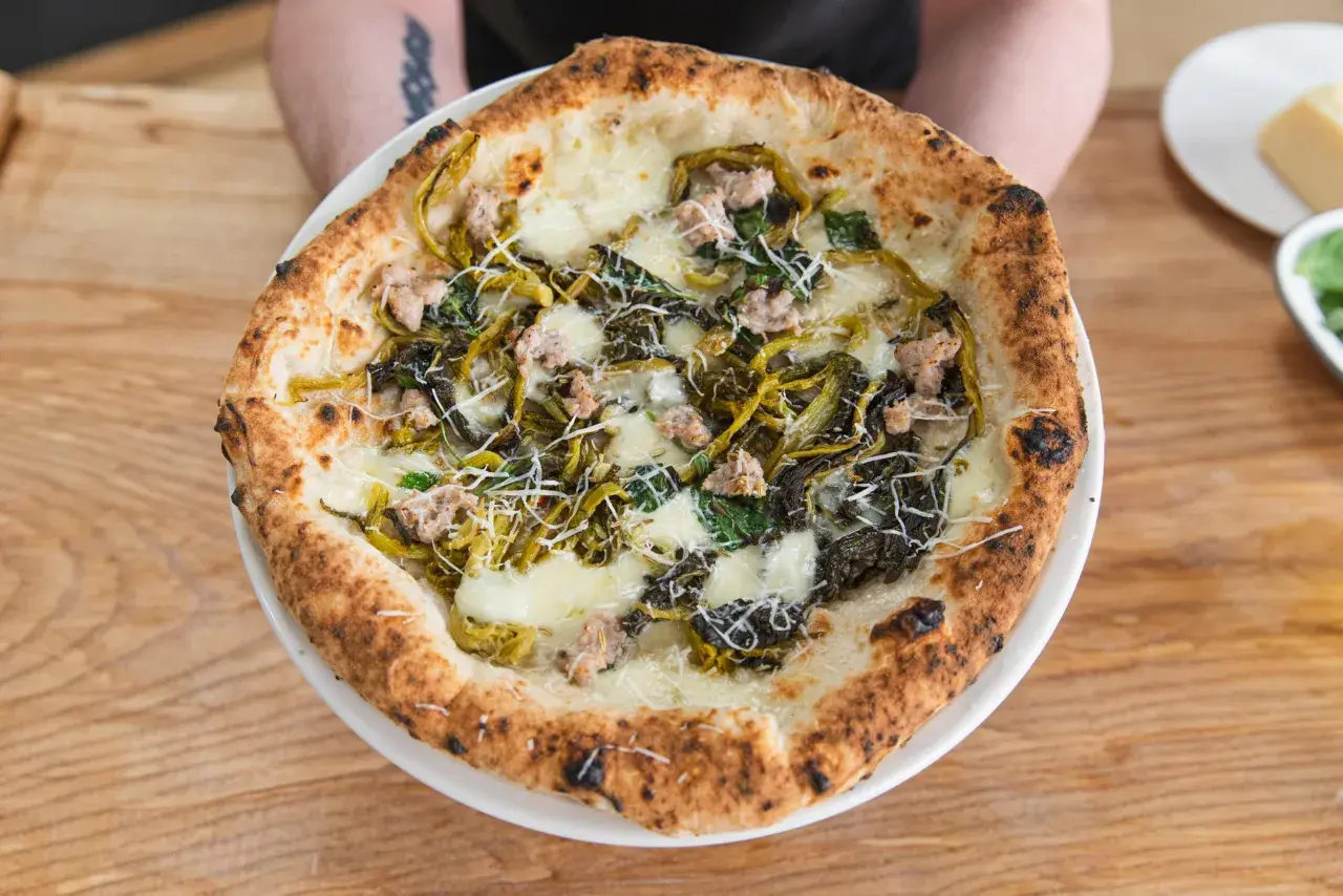 Pizza mit Salsiccia und Friarielli, belegt mit geschmolzenem Käse und geriebenem Parmesan.