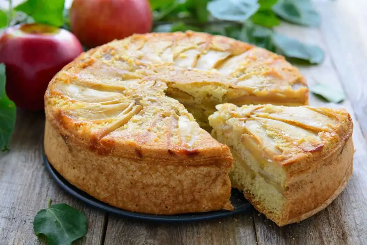 Deliziosa torta di mele vegana con fette di mela disposte a raggiera sulla superficie dorata. Una fetta è già stata servita.