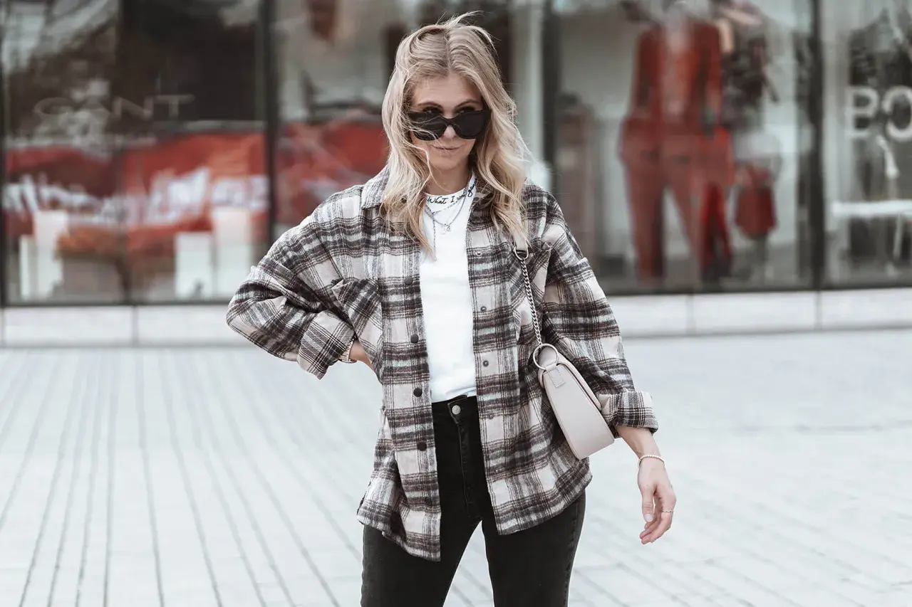 Frau im lässigen Flanellhemd-Style mit Sonnenbrille und Tasche.