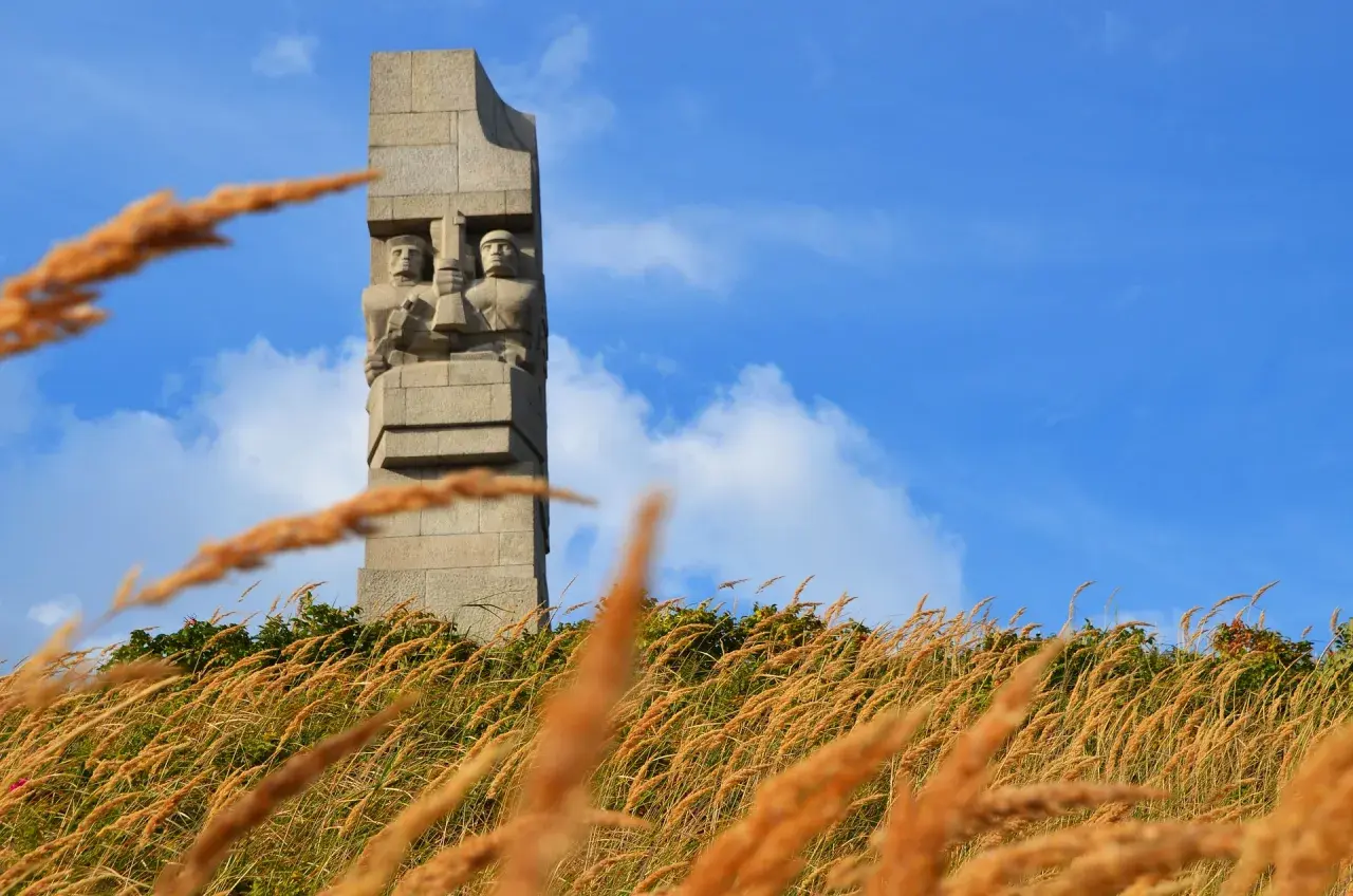 Pomnik Obrońców Wybrzeża na Westerplatte podczas zwiedzania. W oddali widać dwie kamienne postacie żołnierzy.