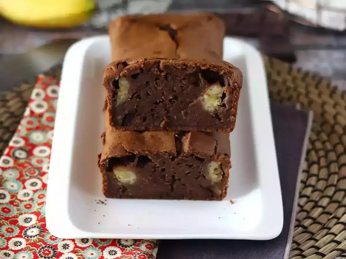 Dos porciones de bizcocho de plátano y chocolate apiladas, con trozos de plátano visibles en su interior.
