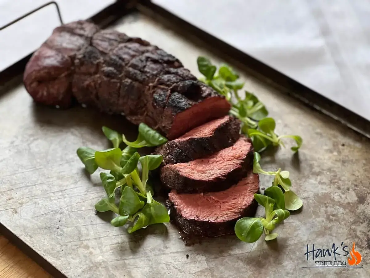 Perfekt grillad oxfilé, saftig och röd i mitten, serverad med färska gröna blad på en rustik plåt. En riktig höjdare för grillmästaren!