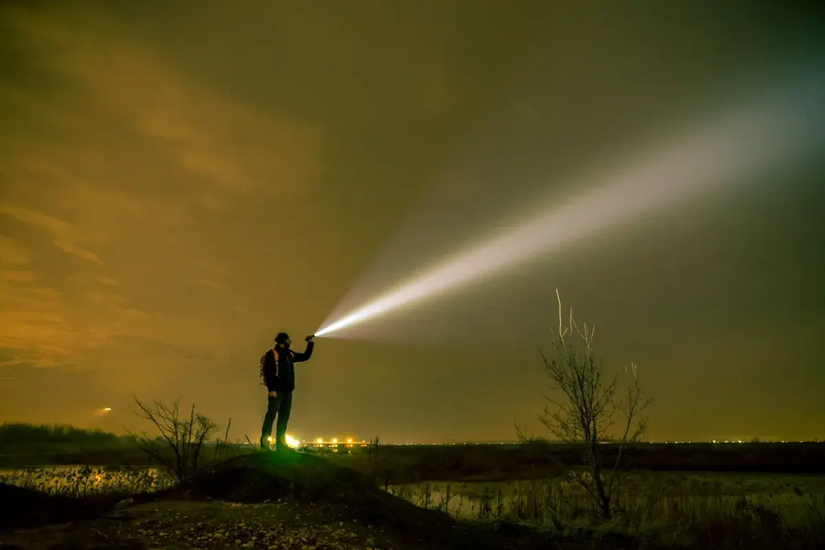 Mężczyzna z plecakiem oświetla nocne niebo potężnym snopem światła z latarki o dużym zasięgu.