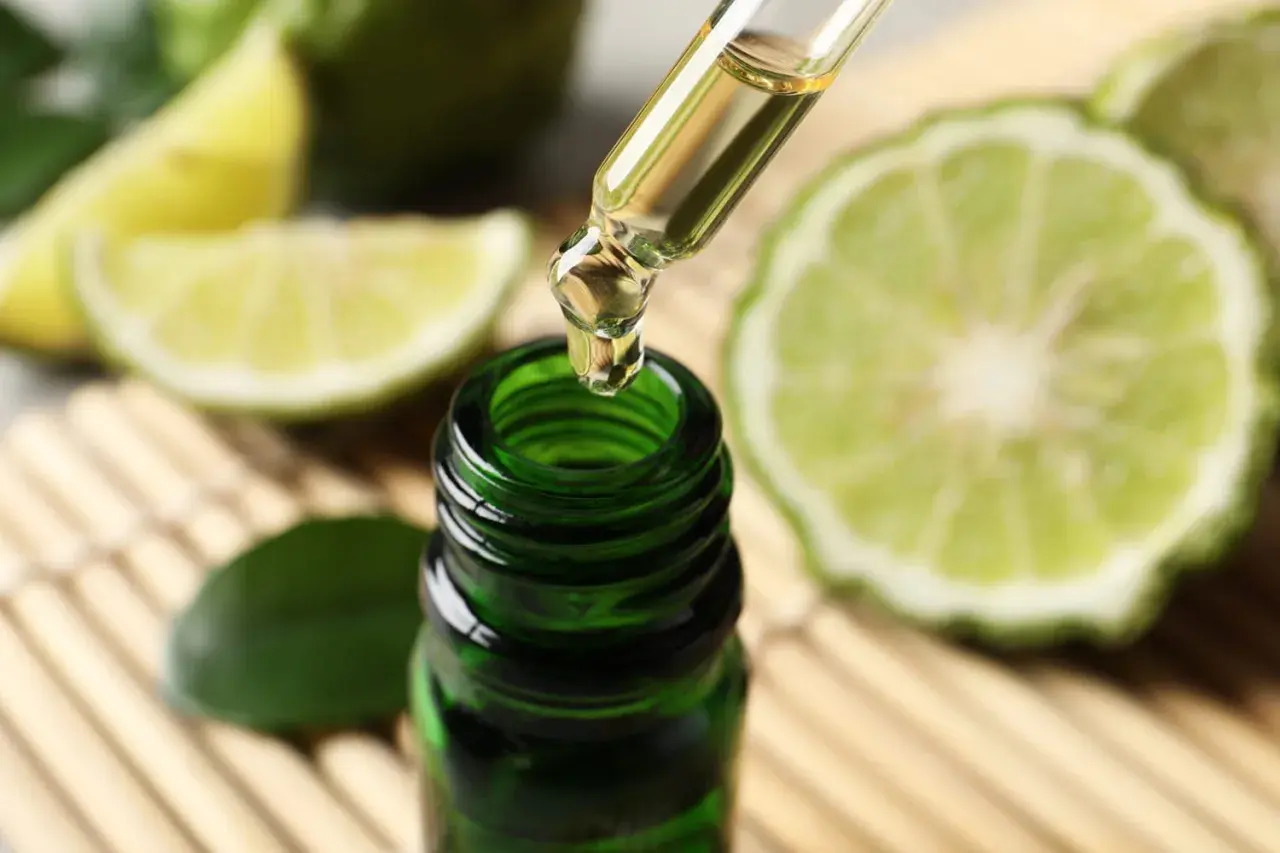 Une goutte d'huile essentielle de bergamote tombe d'une pipette dans un flacon vert. Un remède de grand-mère pour lutter contre la fatigue, entouré de fruits coupés.