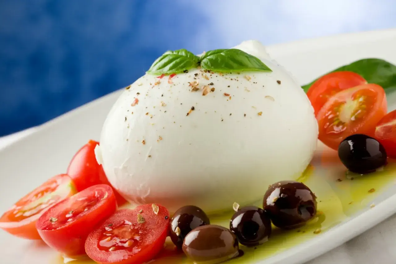 Bufala mozzarella z pomidorkami koktajlowymi i oliwkami na białym talerzu, skropiona oliwą.