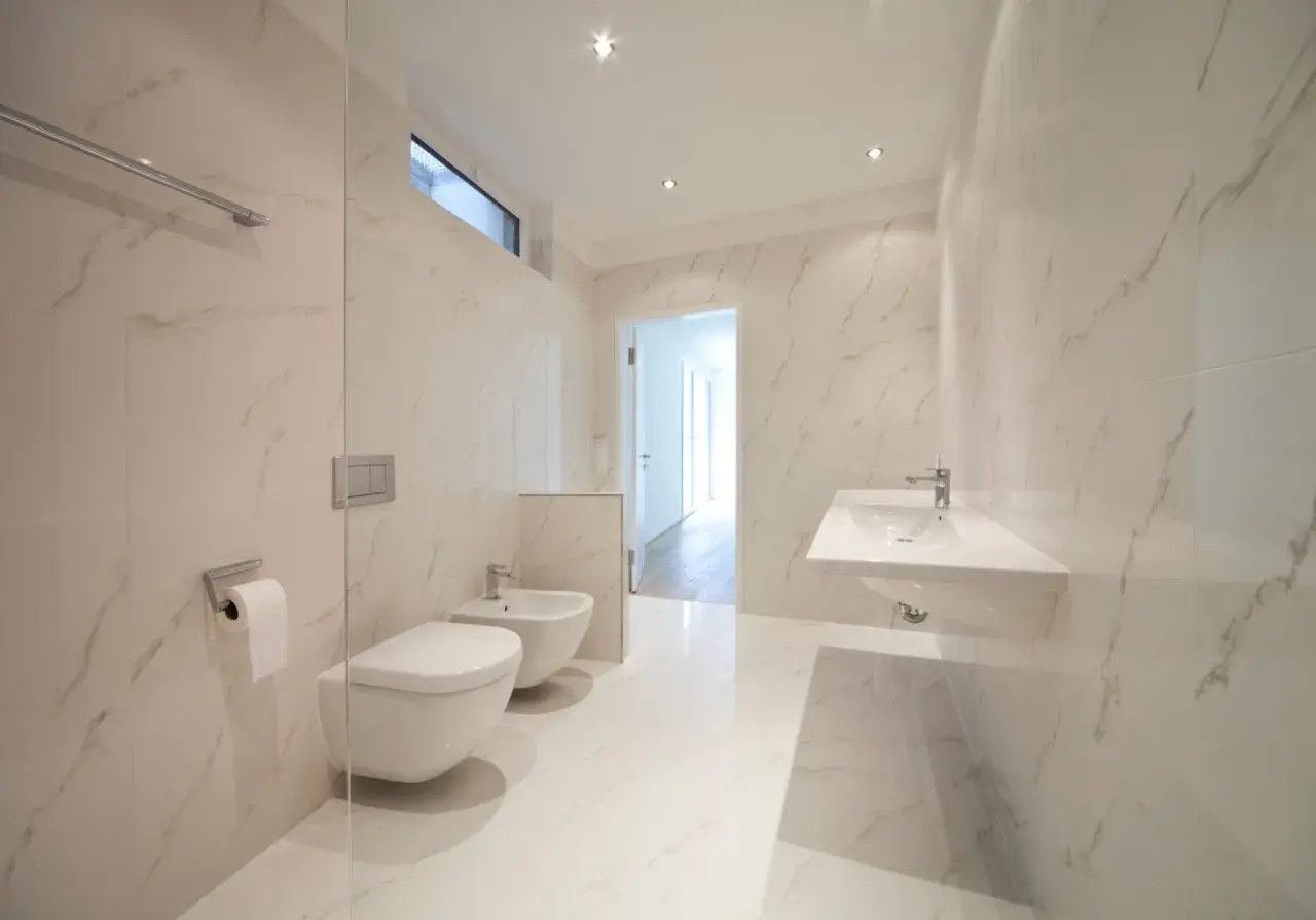 Bagno moderno con bidet e WC sospesi, lavabo a mensola e finiture in marmo. L'altezza scarico bidet è ottimale per un uso confortevole.