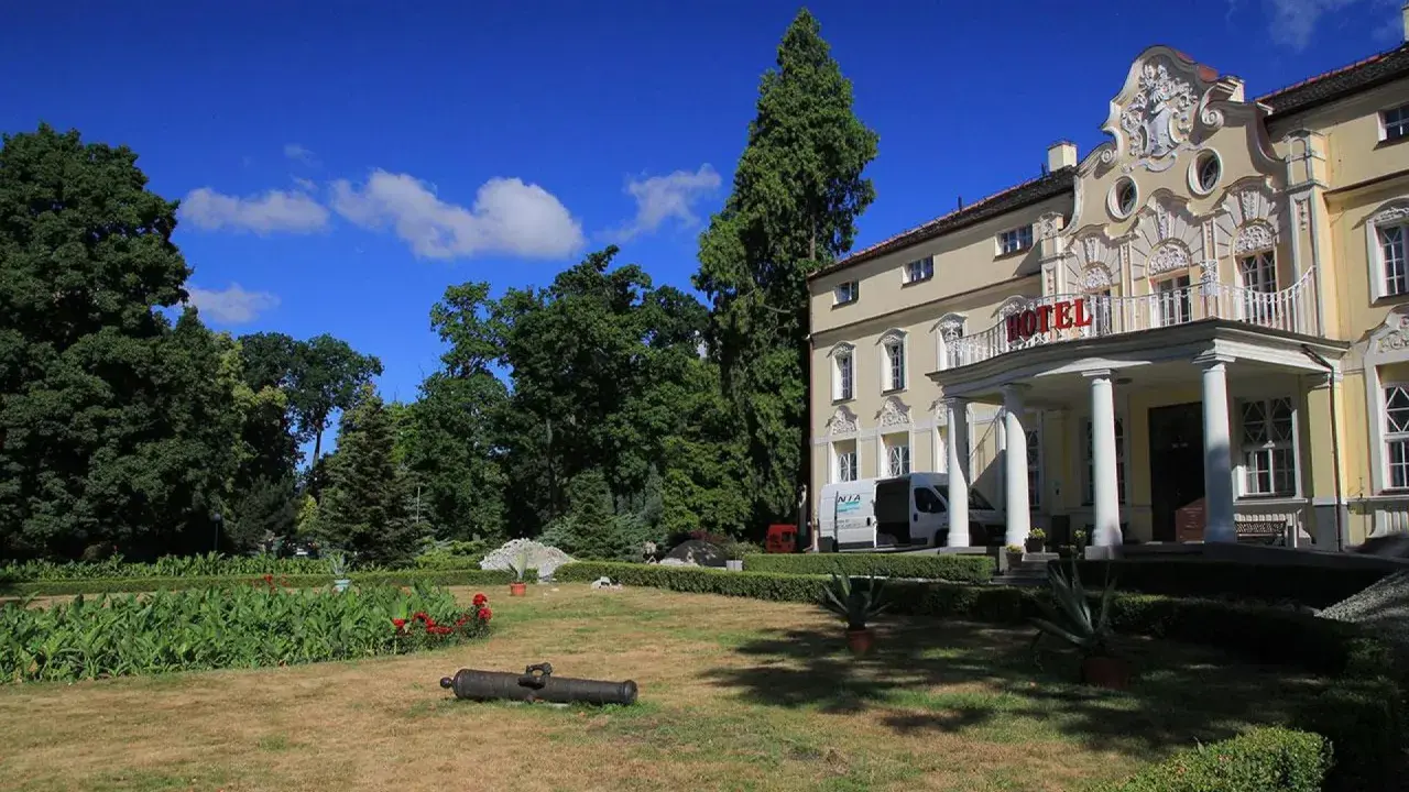 Pałac w Witaszycach, dawniej hotel, otoczony zielenią. Na trawniku leży zabytkowa armata.