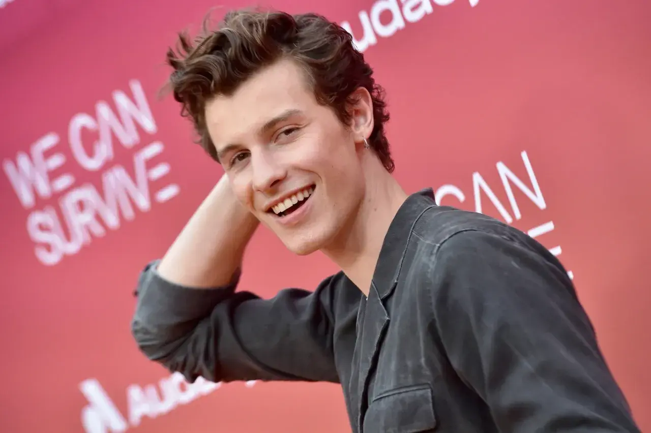 Uśmiechnięty Shawn Mendes na tle napisu "We Can Survive". Czeka na swój **shawn mendes koncert**.